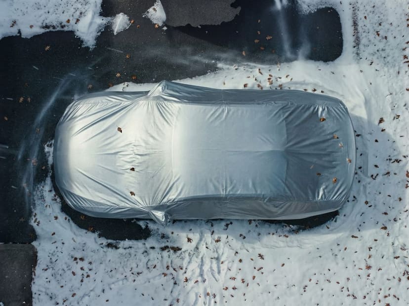 Top-down view of a silver reflective cover fitted over a car on dark pavement with trampled snow.