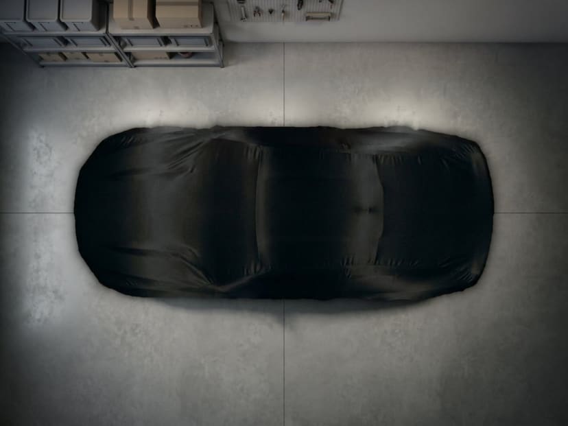 Top-down view of a black stretch cover fitted over a car on a concrete garage floor.