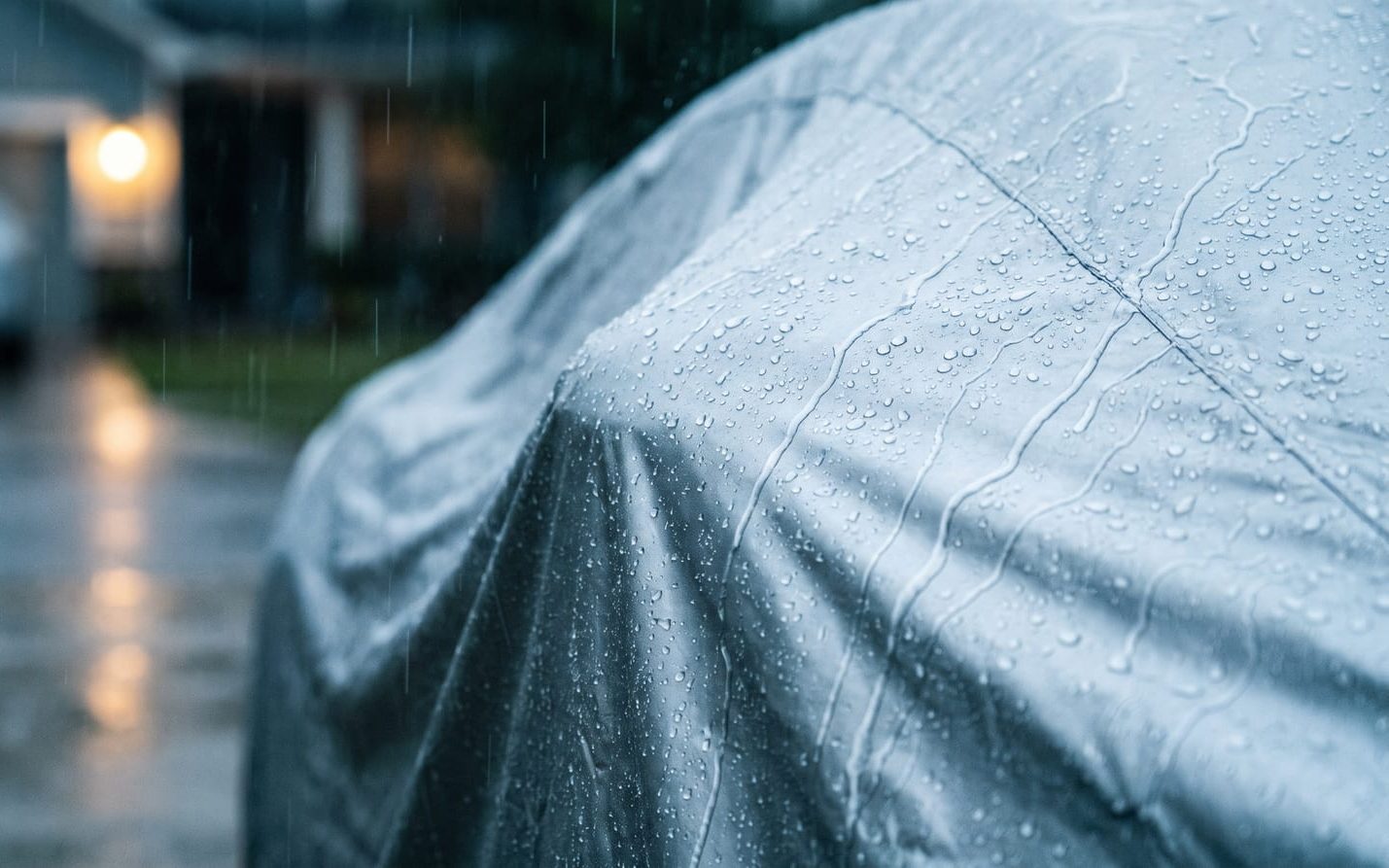 Rain beading and running off a silver outdoor cover on a parked car